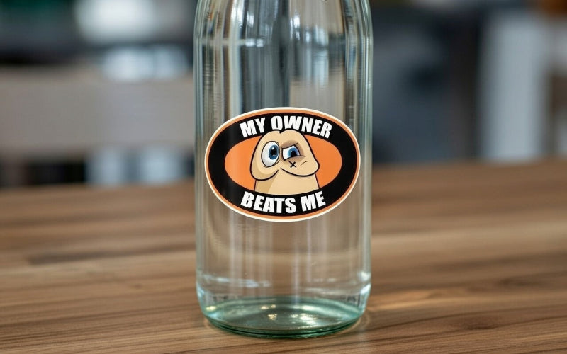 Waterproof sticker of a funny cartoon penis saying 'MY OWNER BEATS ME' adhered to a transparent reusable water bottle.