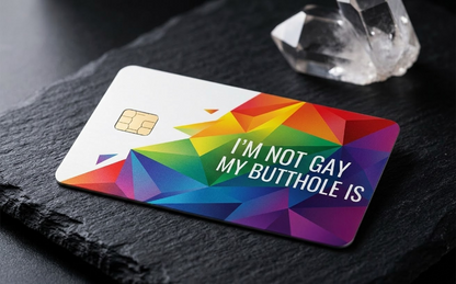 custom geometric rainbow credit cards fanned on a black reflective surface with clear quartz crystals. The cards include a standard chip and white right-aligned text that reads "I'M NOT GAY MY BUTTHOLE IS