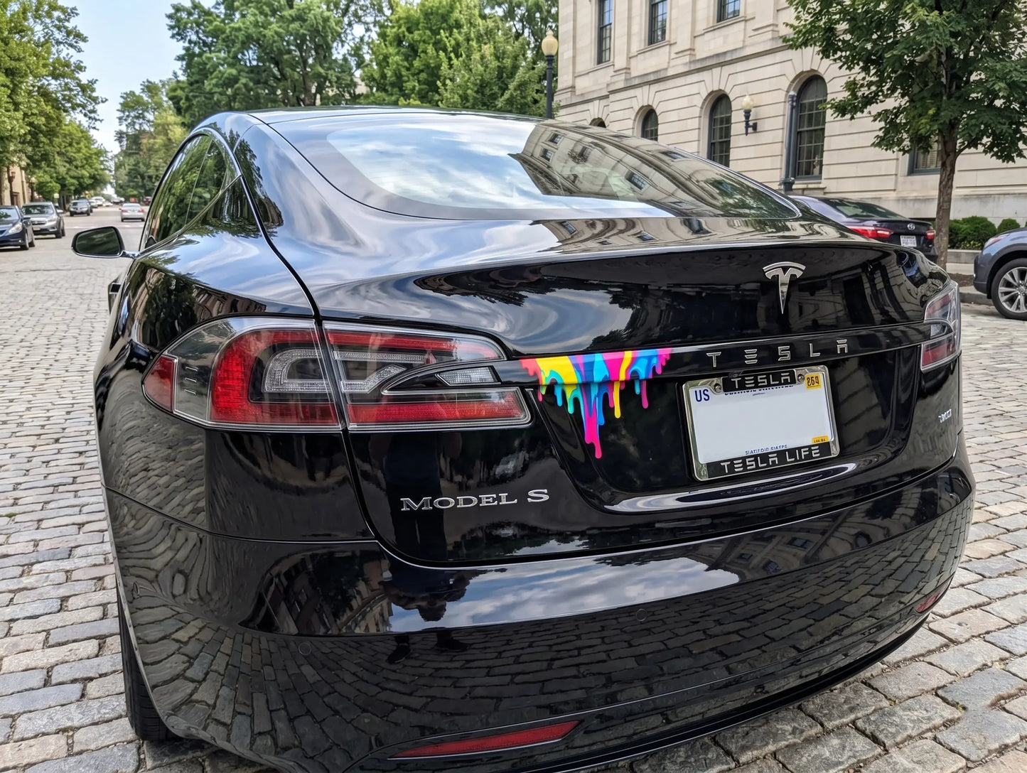 Black Tesla Model S with rainbow paint drip on a city street