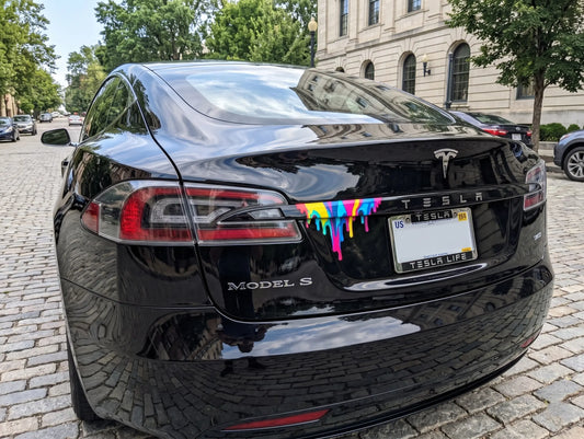 Black Tesla Model S with rainbow paint drip on a city street