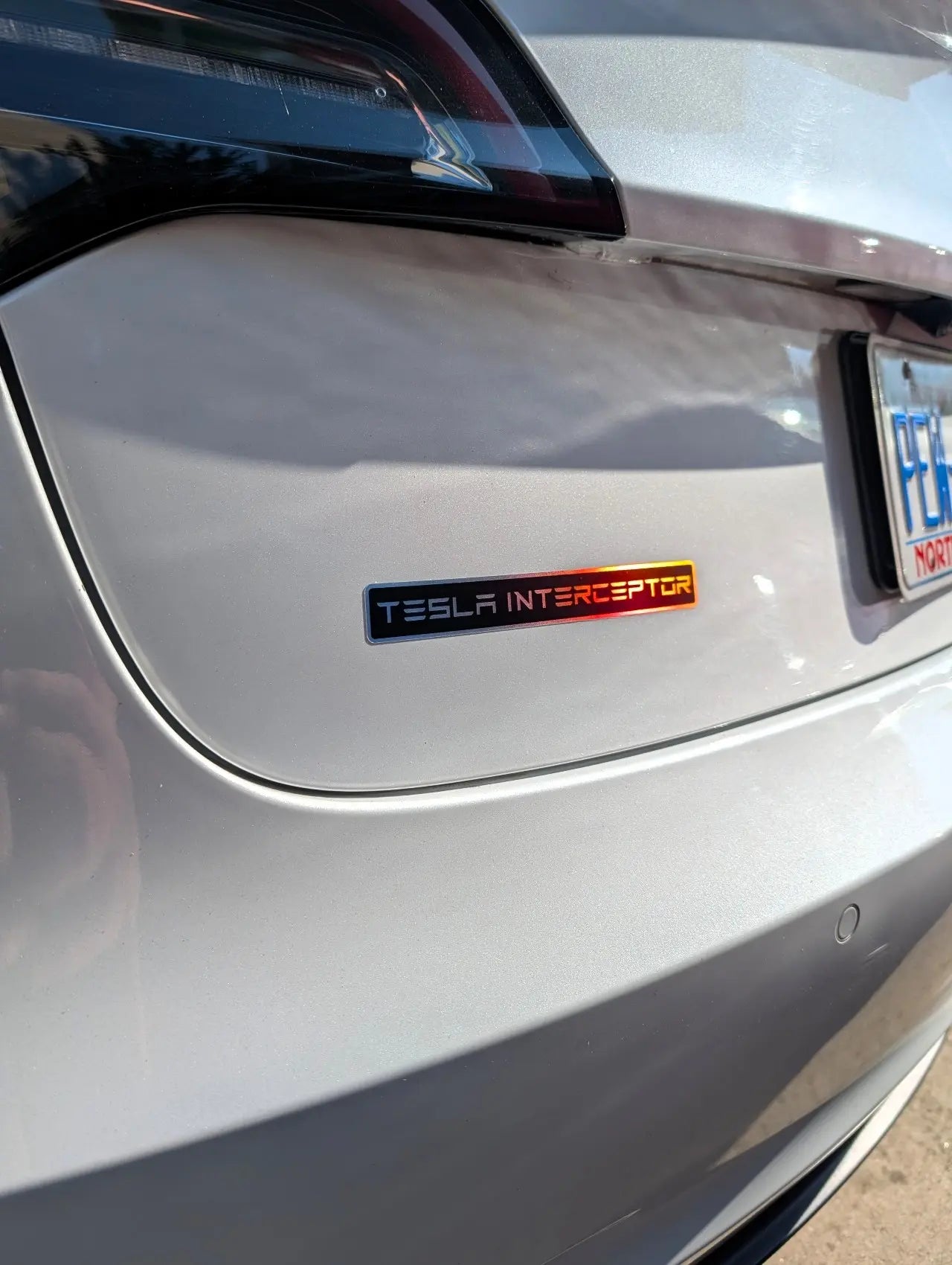 Close-up of a TeslaInterceptor badge on a car, with a visible license plate.